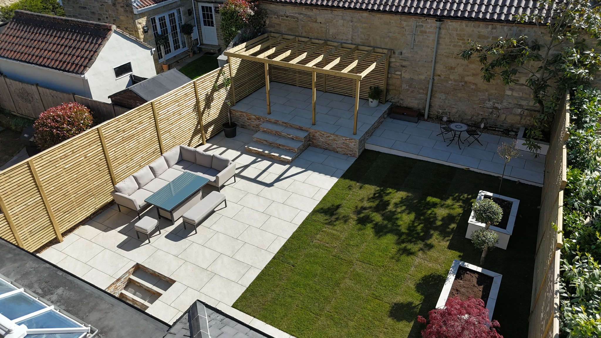 Completed porcelain garden with timber pergola, raised terrace, steps, seating area and lawn